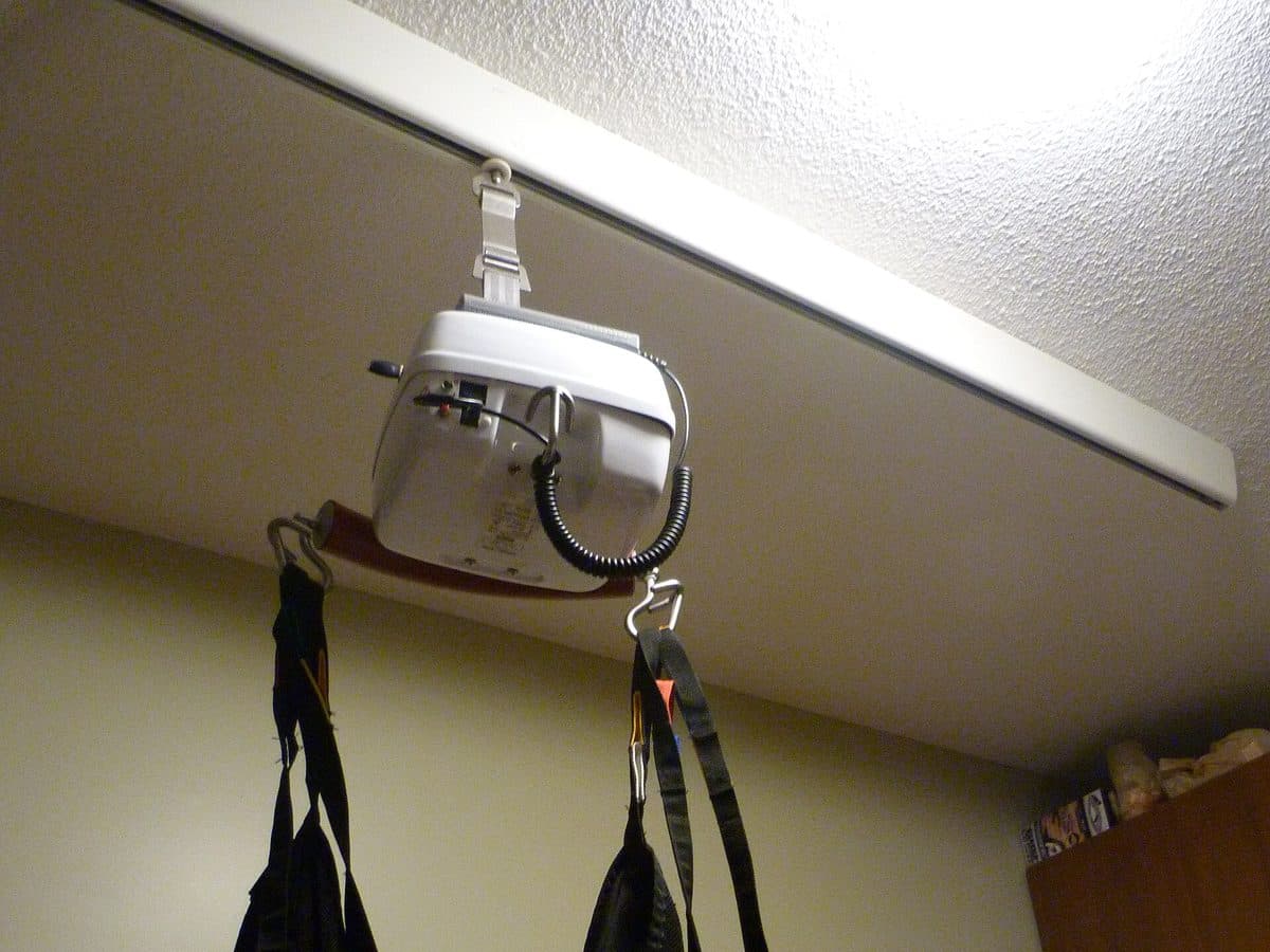 Ceiling hoist motor running on an overhead track, with a transfer sling attached