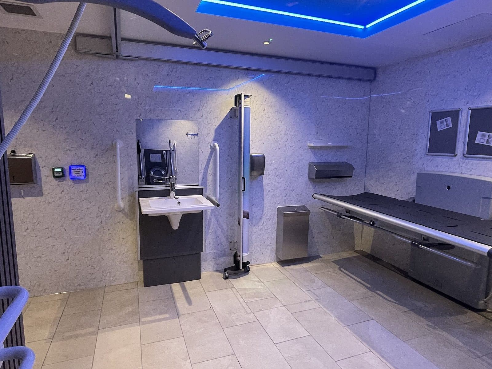 Accessible bathroom with a ceiling hoist track, an adult change table and grab rails