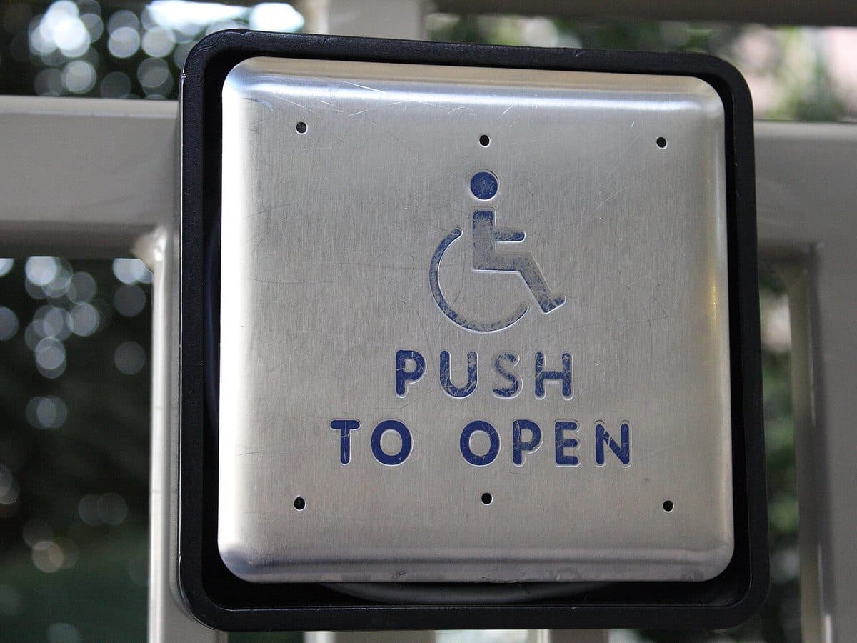 Wall-mounted 'Push to open' button for an automatic door, marked with the international symbol of access